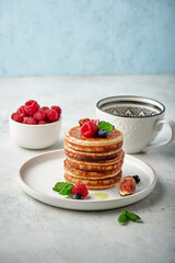 Tasty appetizing homemade pancakes served with honey, raspberries and blueberries on plate on grey background