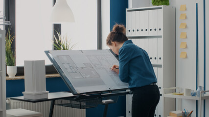 Close up of woman architect taking notes on blueprints plans to design building layout. Engineer...