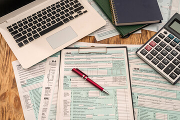 on  wooden table are tax forms 1040, calculator, laptop pen notebooks