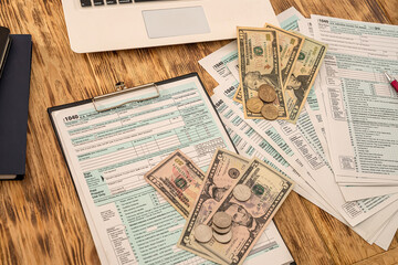 Naklejka premium white laptop tax form usa 1040 with dollar bills and coins spread out on a wooden table