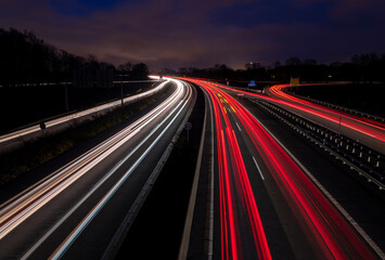 Night view of German Autobahn “A40“ in Ruhr Basin Germany in Duisburg-Kaiserberg near Oberhausen, Essen and Duesseldorf. Panoramic longtime exposure with red and white lights of passing cars at dusk.