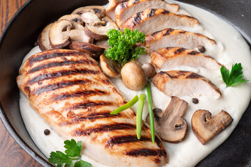 Roasted chicken fillet and mushrooms with herb in the frying pan on the wooden table close-up.