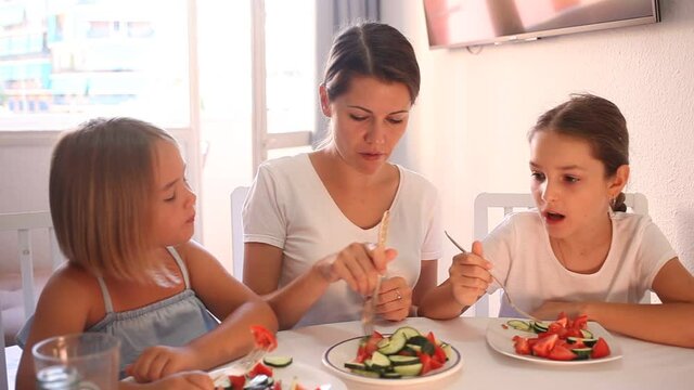 Young mother and two daughters eating healthy food with vegetables in living room