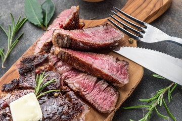 Medium rare Ribeye steak with herbs and a piece of butter on the wooden tray.