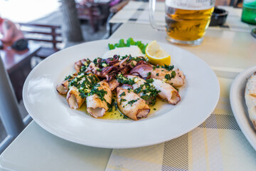 Grilled squids with herbs, garlic and lemon on white plate close-up. Popular and delicious Mediterranean meal.
