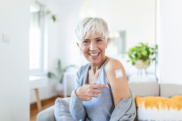 Woman pointing at her arm with a bandage after receiving the covid-19 vaccine. Mature woman showing her shoulder after getting coronavirus vaccine