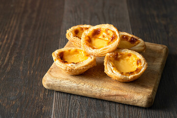 Many  Pasteis de Belem or  pastel de nata on wooden cut board.