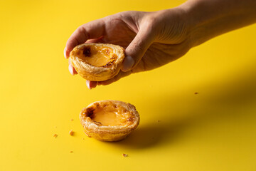 Female hand holding typical Portuguese sweet , pasteis de belem  on yellow backgorund