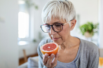 Sick woman trying to sense smell of half fresh orange, has symptoms of Covid-19, corona virus infection - loss of smell and taste. One of the main signs of the disease. - obrazy, fototapety, plakaty