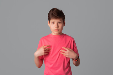 Handsome teenager boy pointing hands at himself, standing over gray background, having doubtful confused uncertain facial expression