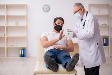 Fototapeta premium Young male patient visiting old doctor in vaccination concept