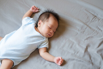 Asian baby sleeping on gray bed