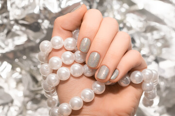 Female hand with glitter silver nail design. Female hand hold white glass beads. Glitter silver nail polish manicure.
