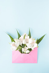 Flowers in a pink envelope on a blue background. Spring aesthetic concept with vibrant colors.