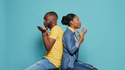 Frustrated man and woman sitting back to back and having argument in studio. Couple in conflict...