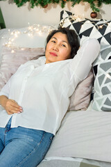 Senior asian woman rest on bed with xmas decoration and lights, elderly smiling lady relaxing at home at Christmas