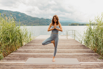 Woman doing tree pose while meditating on jetty