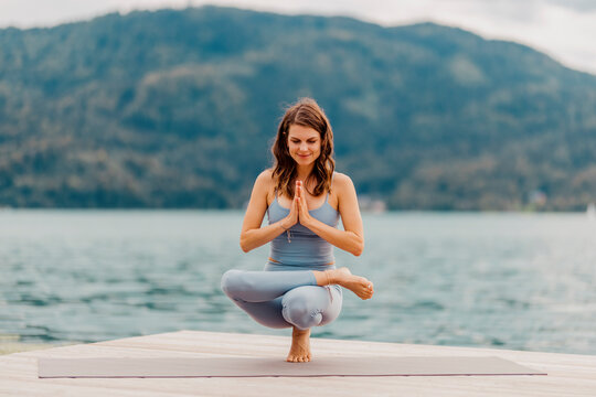 Smiling woman practicing toe stand on jetty in front of lake