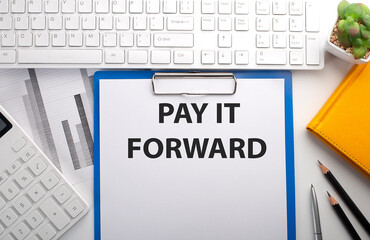 PAY IT FORWARD written on the paper with keyboard, chart, calculator and notebook