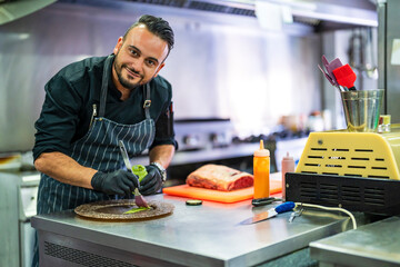 Smiling chef decorating plate for presentation in kitchen of restaurant