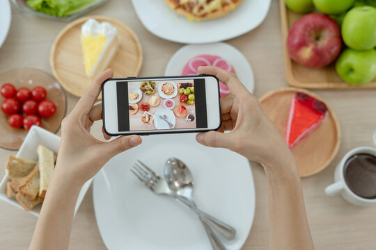 A man uses a mobile phone to open an app to take pictures of food at a table in a restaurant.