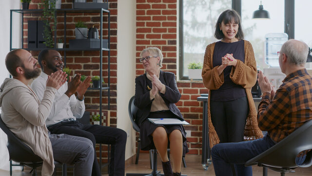 Happy Adult Celebrating Recovery Success With Group Of People Clapping Hands At Aa Meeting. Woman Sharing Achievement And Progress At Therapy, Receiving Applause From Addiction Patients.