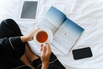 Young black woman drinking tea and reading magazine while sitting in bed