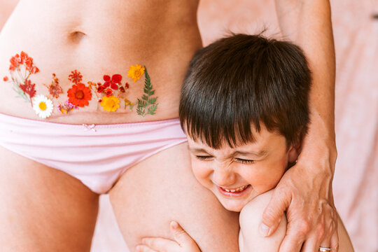 Happy son embracing mother with flower tattoo on Caesarean scar