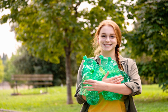 Smiling female volunteer holding plastic bottles in garden - Powered by Adobe