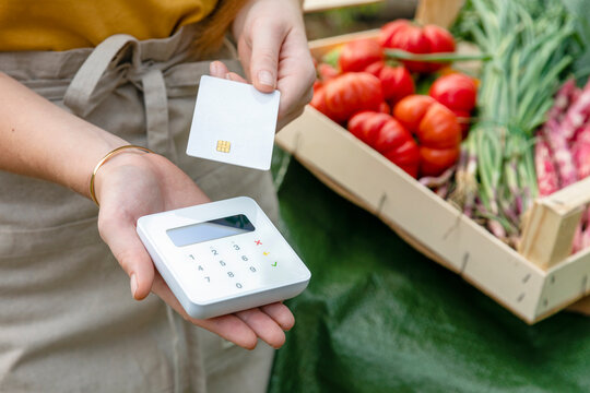 Female farmer with credit card holding wireless card reader by vegetable's crate