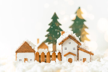 Happy New Year and Merry Christmas postcard. Festive white background with toy wooden house, snow, light bokeh, christmas tree, village and decoration. Copy space for winter holidays greeting card. 