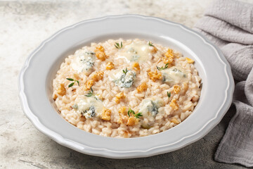 Close-up of gorgonzola and walnut risotto decorated with thyme in light grey plate. Traditional...