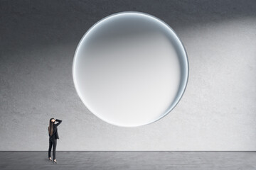 Obraz premium Businesswoman standing in minimalistic concrete interior with abstract clean round poster on wall. Mock up. Exhibition, gallery and art concept.