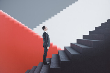 Attractive young european businessman standing on red and concrete staircase with mock up place. Success, finance and career growth concept.