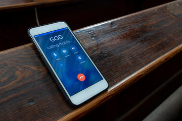 Calling God with a mobile phone on the table of a prayer bench in the church, close up.