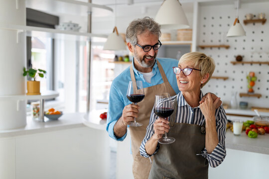 Happy senior couple cooking together and drinking wine in home kitchen