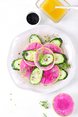 Salad with watermelon radish, cucumber, microgreen, black salt and lemon dressing with olive oil on the ceramic plate. Healthy vegan meal. Top view
