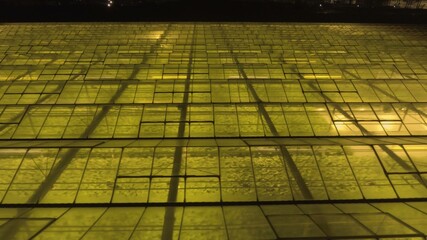 Abstract green geometric background. Illuminated greenhouses at night. Agricultural infrastructure on glass roofs.