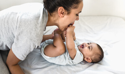 Happy mother playing with her baby lying together on bed