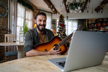 Portrait of a man taking guitar lessons online in a room at home