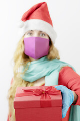 A box with a Christmas present in the girl's hand. A woman in a Santa Claus hat in a medical mask and gloves. Full protection for Christmas. Sterile gift. Focus on the gift
