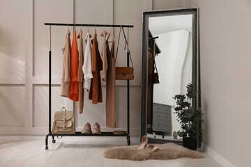Rack with stylish women's clothes and mirror in dressing room