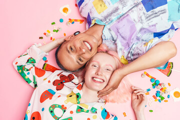 Young couple hugging and smiling while lying with candies on floor