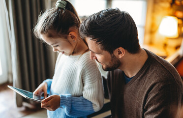 Happy father and daughter using digital tablet at home. Family, people, technology concept