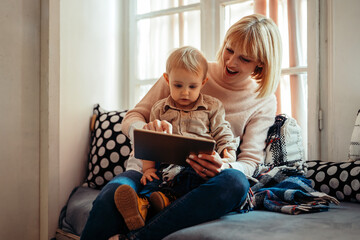 Happy family technology concept. Smiling mother and her toddler son playing with digital tablet