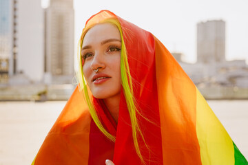 Young white woman looking aside while standing with rainbow flag