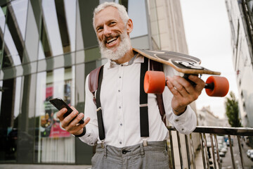 Grey mature man using cellphone while standing with skateboard © Drobot Dean