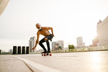 Grey mature man with beard skateboarding on parking