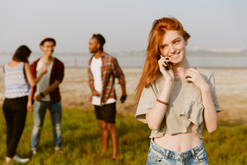 Young ginger woman smiling and talking on cellphone outdoors