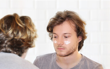 young man taking care of his undereye wrinkles applying facial mask. Applying the cream